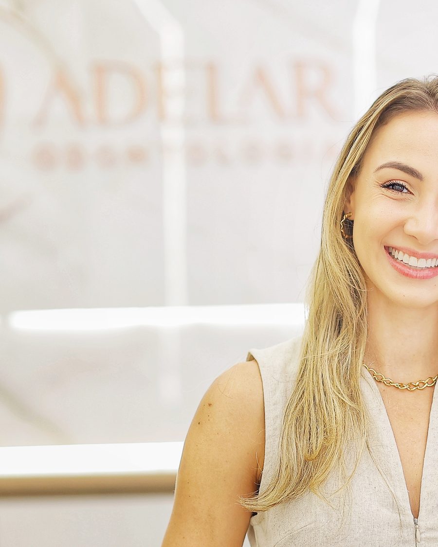 Dra. Mariana Adelar, responsável técnica, em frente ao painel com o logo da Adelar Odontologia